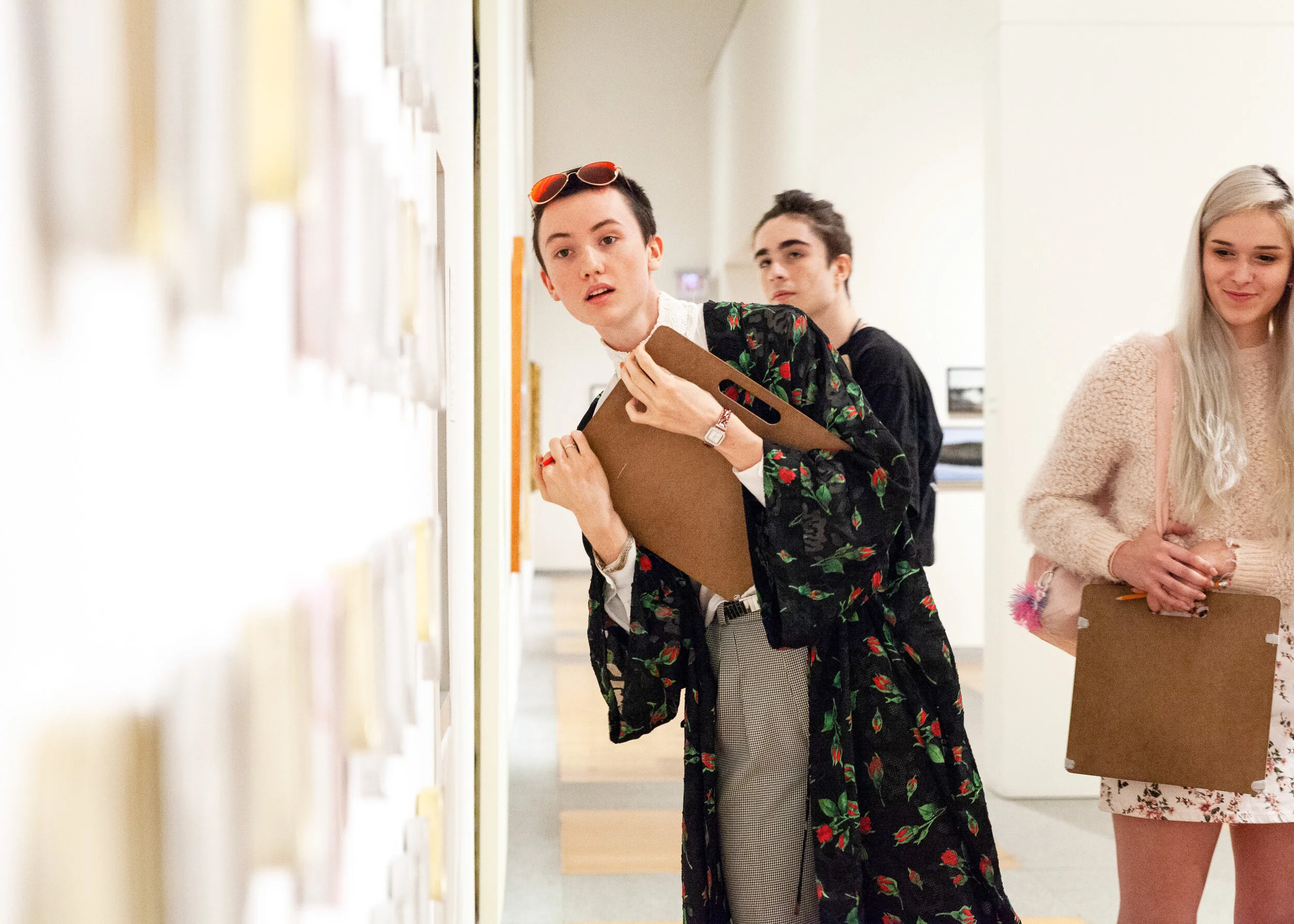 Three people observing artwork in a gallery, one looking intrigued.