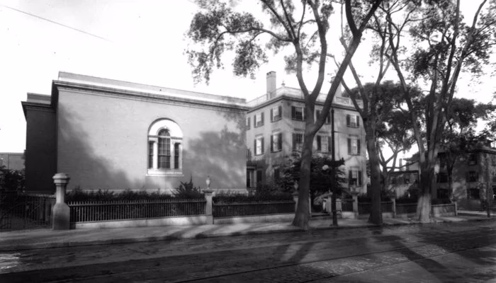 Historic black and white tree-lined street with classic buildings.