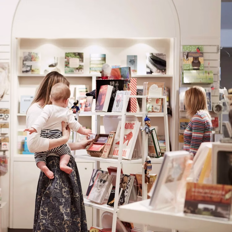 Woman holding a baby browses books in the PMA store.