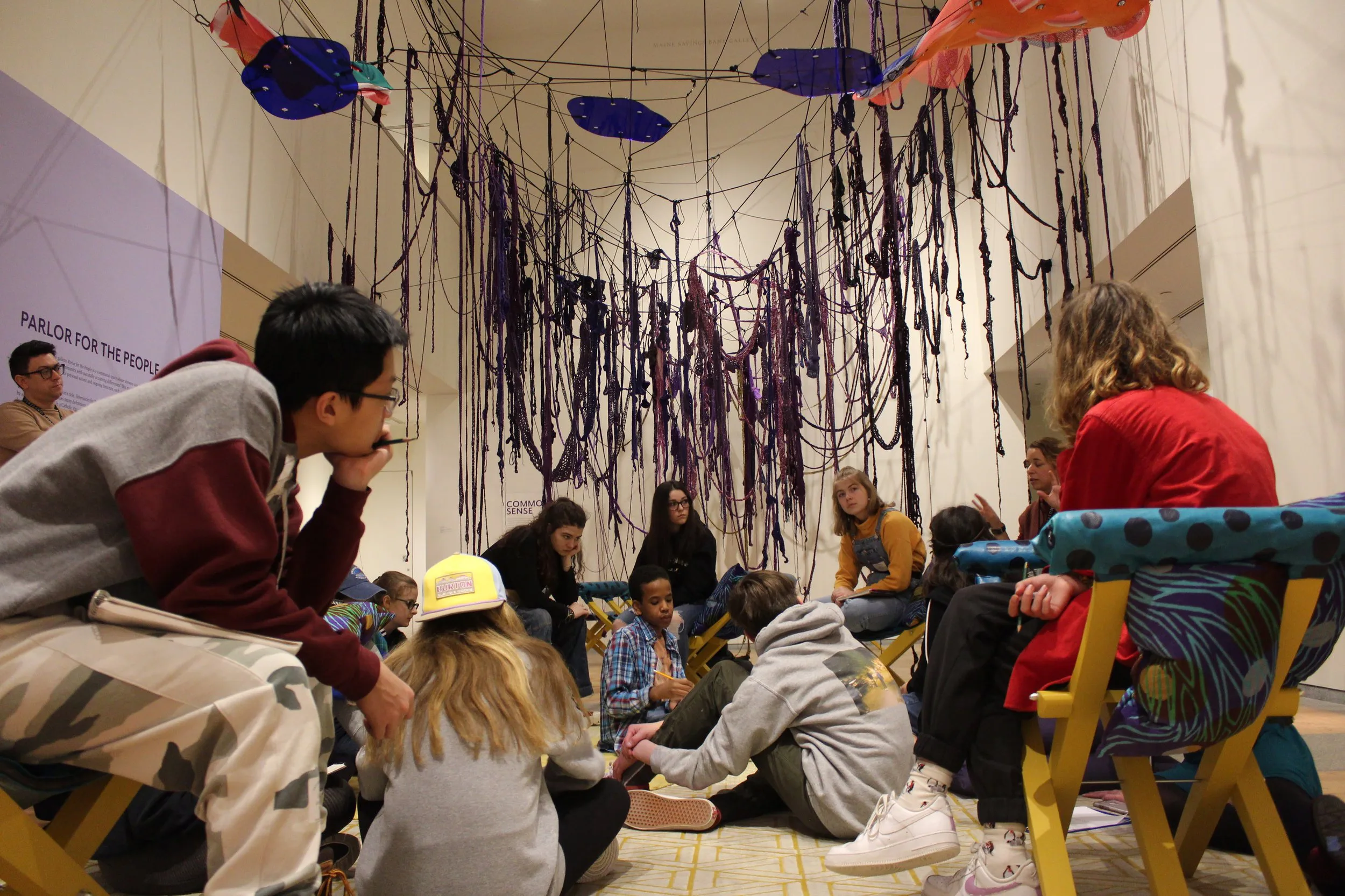 Group of people sitting under a ceiling decorated with purple streamers.