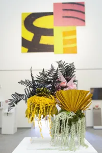 Colorful abstract paintings above a vibrant floral arrangement in an art gallery.