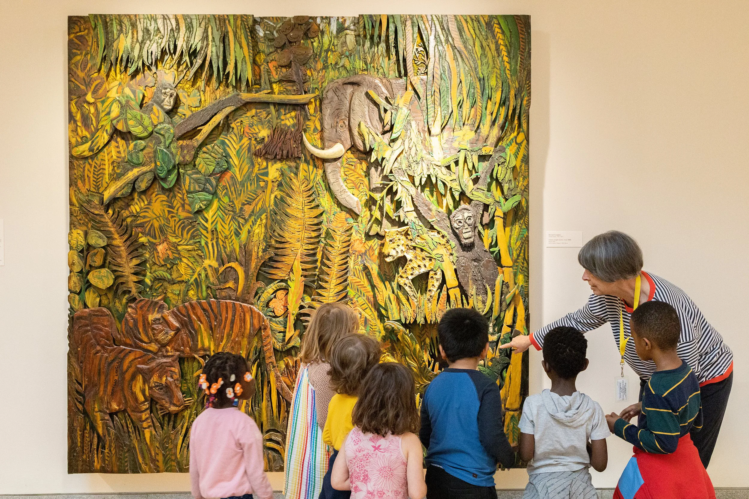 Teacher guiding children viewing a colorful jungle-themed artwork in a museum.
