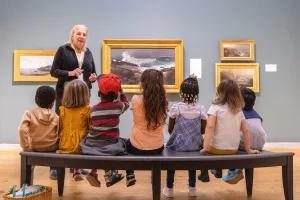 Woman teaching a group of diverse children at an art gallery.